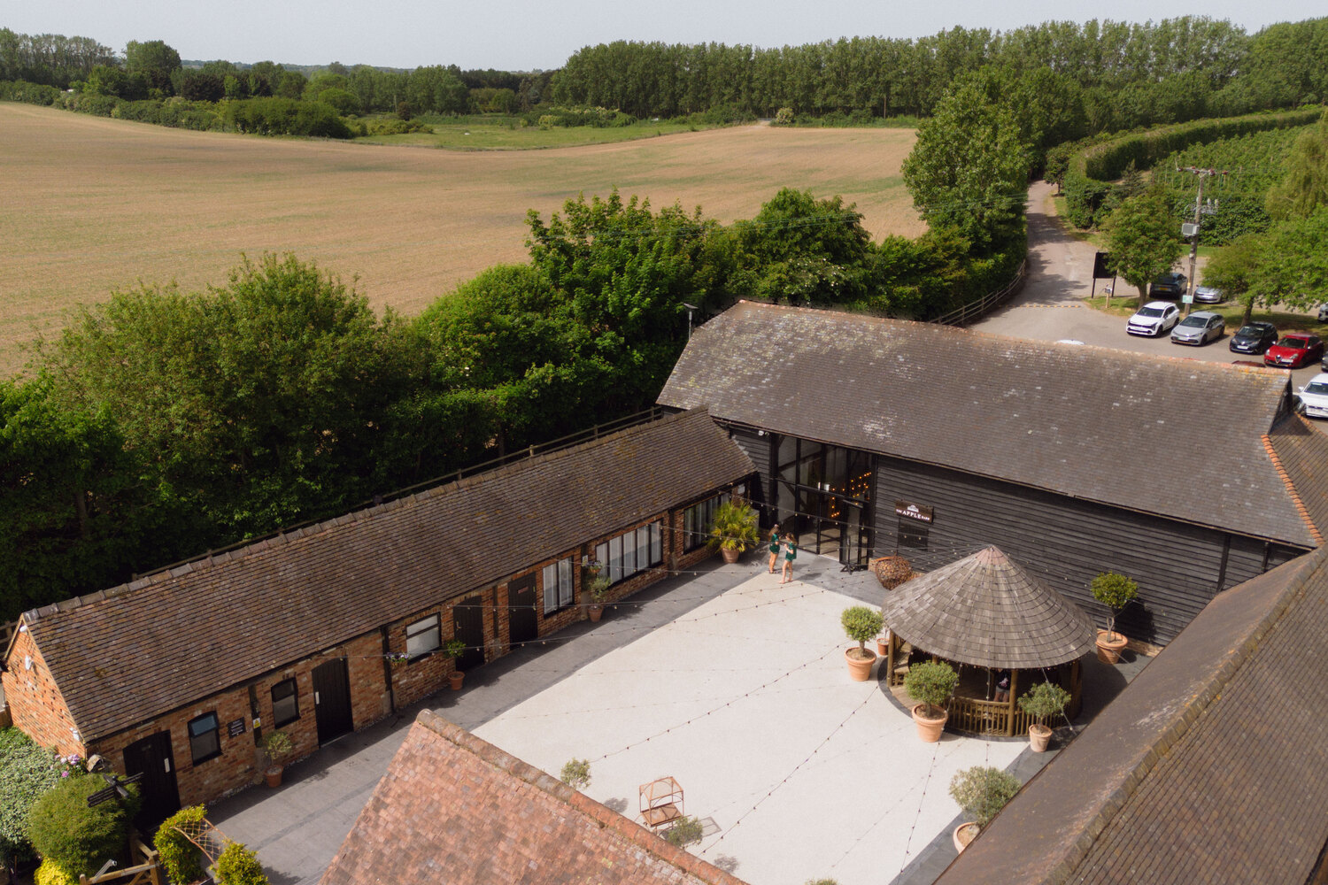 Aerial view of the Courtyard, the Apple Barn and the orchards at The BarnYard, with the car park alongside