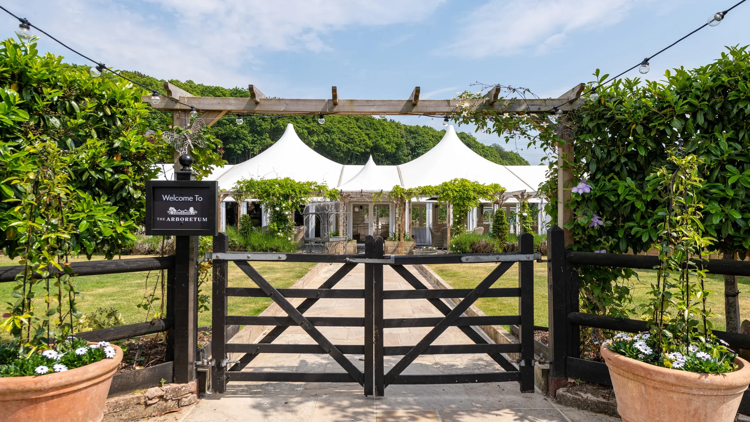 The gated entrance to The Arboretum at The BarnYard, a pergola walk leading to the glass pavilion