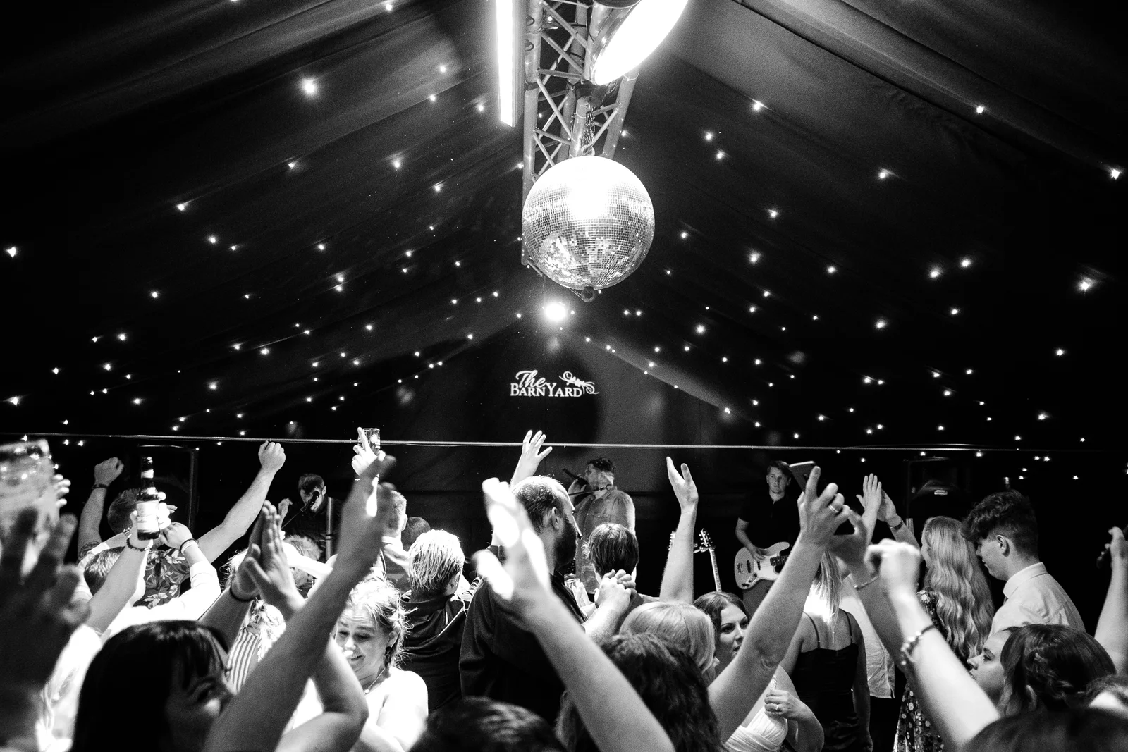 A packed dancefloor at The BarnYard with hands in the air, a mirrorball turning under the star-lit ceiling and a live band playing