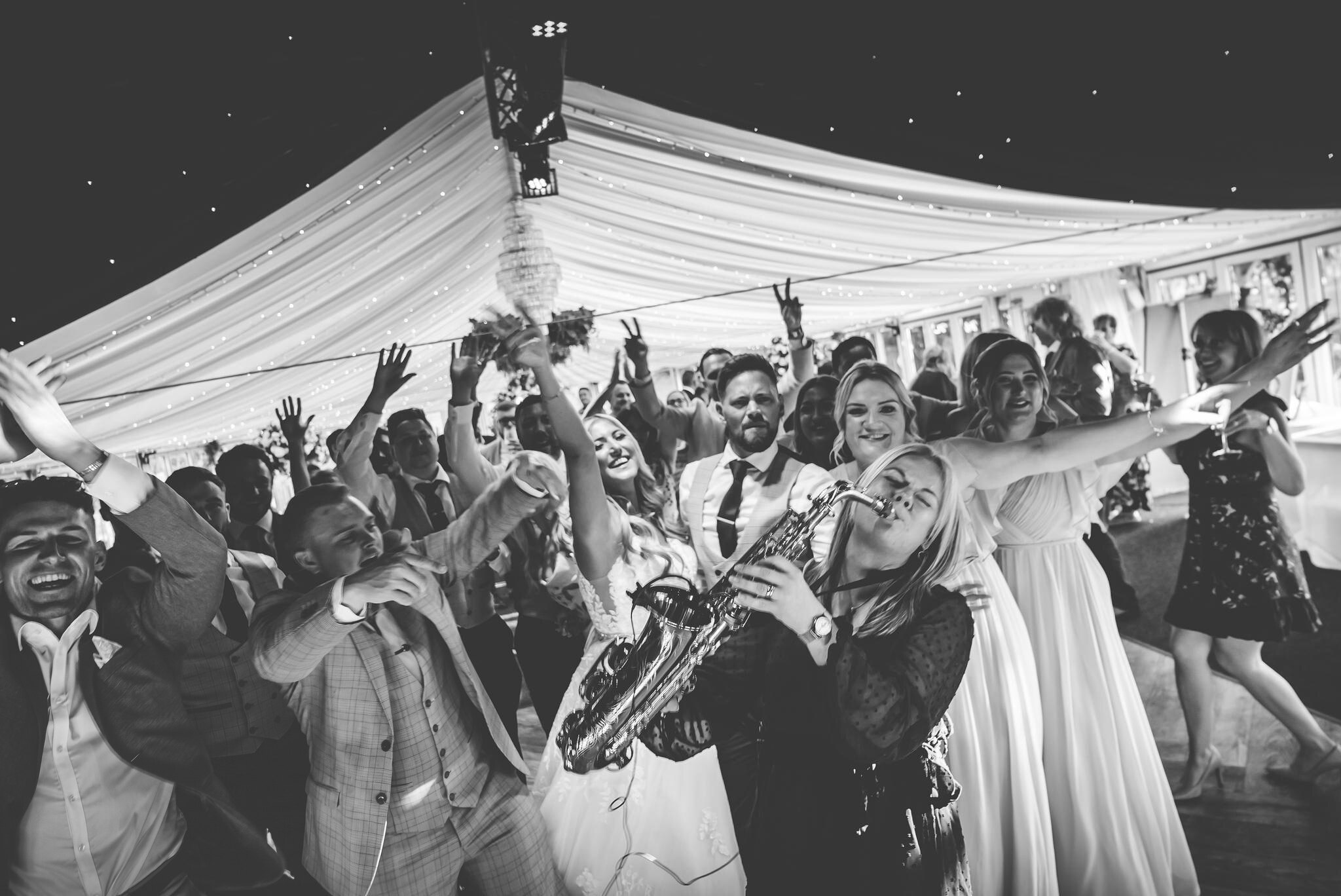 A packed dancefloor at The BarnYard, a saxophonist playing among the guests under the fairy-lit ceiling