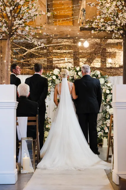 A bride's long veil trails behind her as she reaches the altar in the Apple Barn