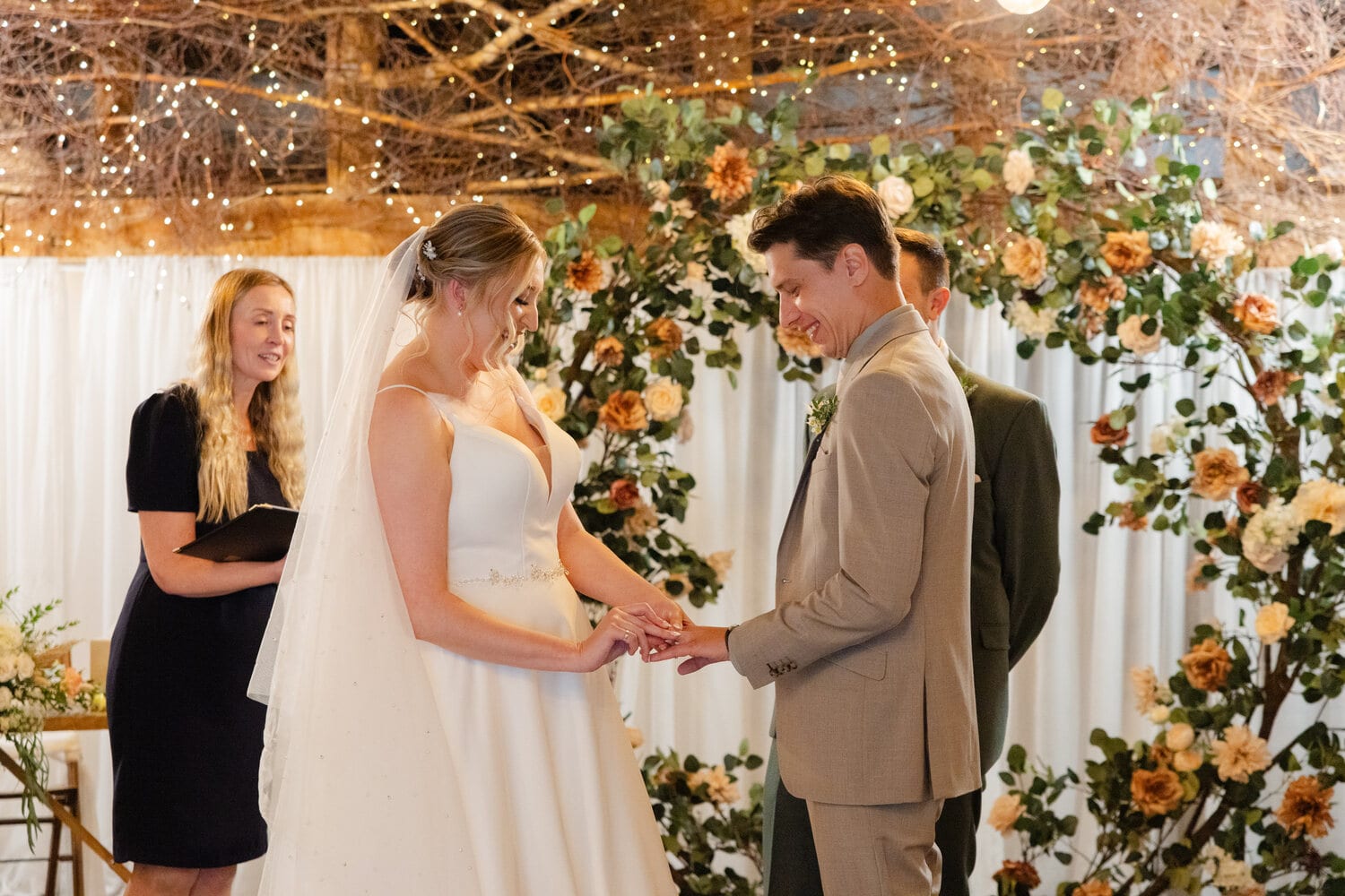 A couple say their vows under a greenery arch in the Apple Barn