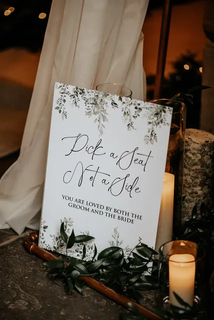A 'Pick a Seat Not a Side' sign framed with white florals at an Apple Barn ceremony
