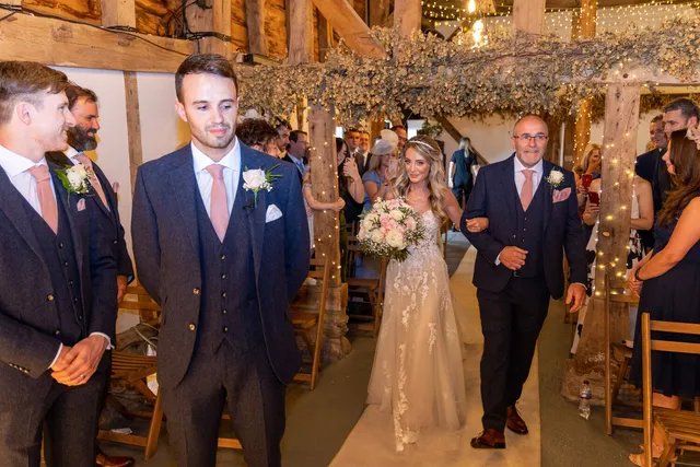 A bride walks the Apple Barn aisle with her father as guests look on