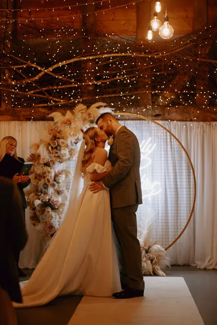 A couple share their first kiss beneath a circular pampas arch in the Apple Barn