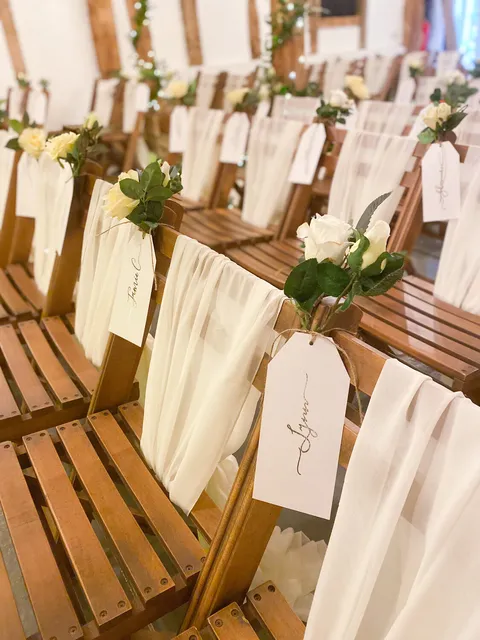Ceremony chairs dressed with ivory sashes, foliage and name tags in the Apple Barn