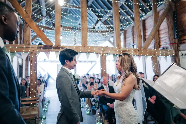 A couple exchange rings in the Apple Barn with bunting and guests behind