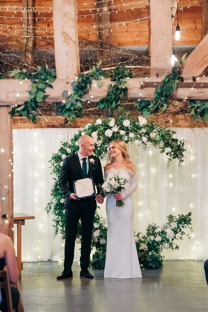 A bride reads her vows beneath the greenery arch in the Apple Barn