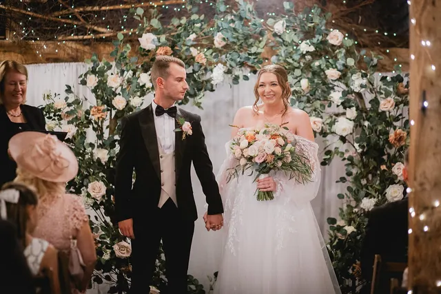 A newly married couple walk back down the aisle beneath a floral arch in the Apple Barn