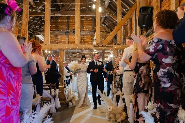 A couple walk back down the aisle as guests applaud in the Apple Barn