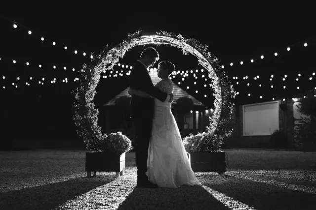 A couple framed in a ring of fairy lights, in black and white