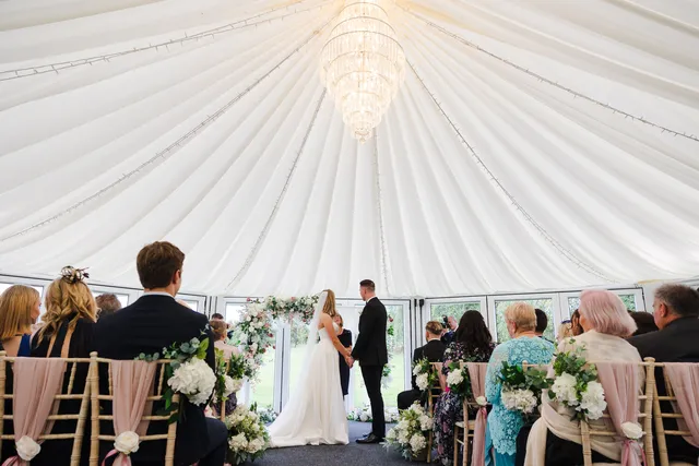 A couple at the altar inside the Arboretum, the draped ceiling and chandelier above