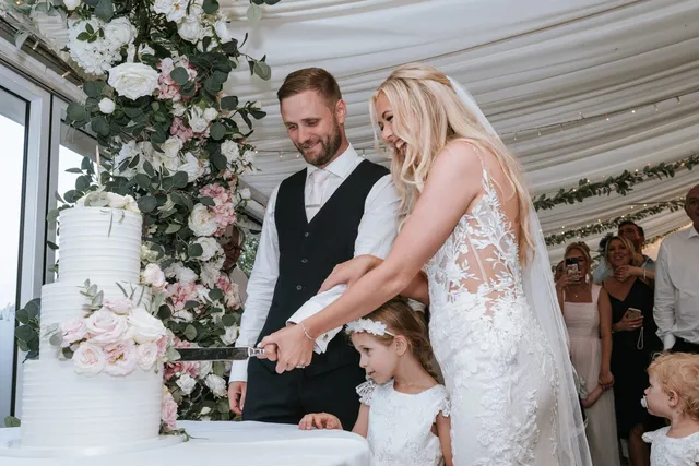 Cutting the wedding cake with a flower girl watching