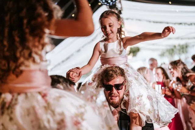A flower girl riding on a guest's shoulders