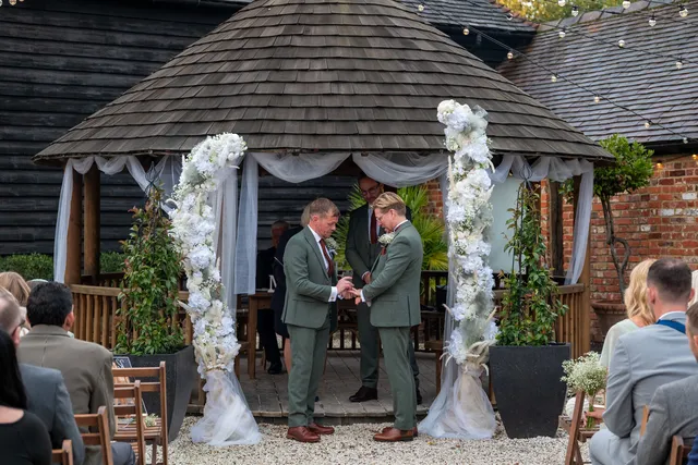 A couple exchange vows beneath white florals at the Courtyard gazebo