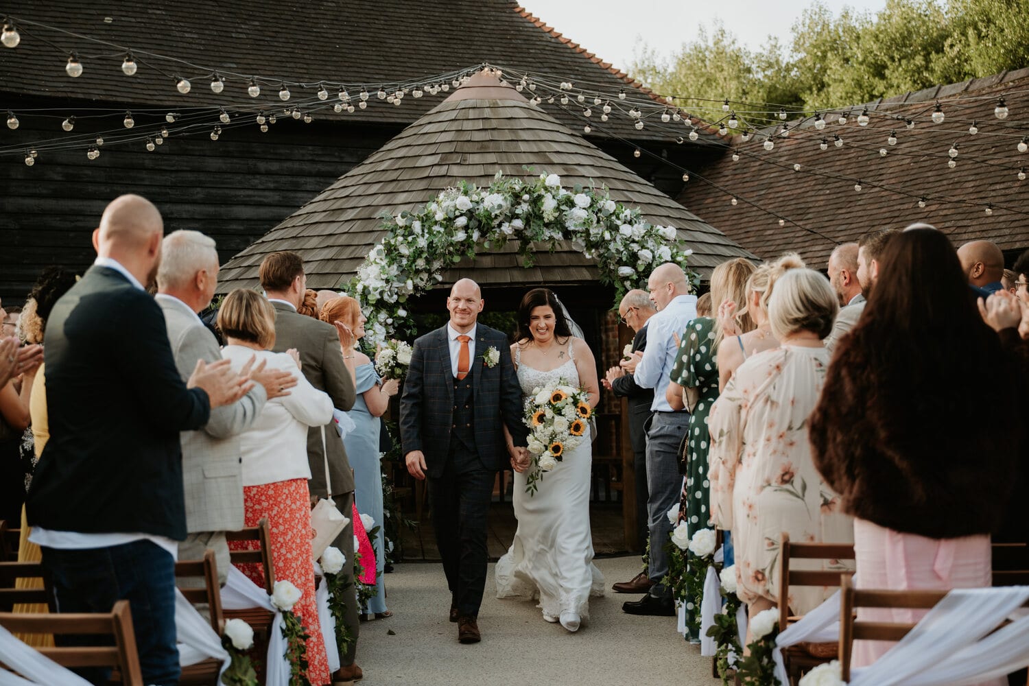 A couple and guests at a courtyard ceremony by the barns