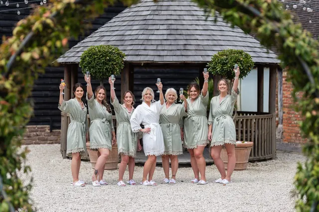 Bridesmaids in sage robes raising a toast outside