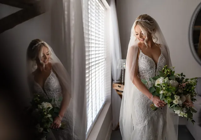 A bride at the window in her dress, bouquet in hand
