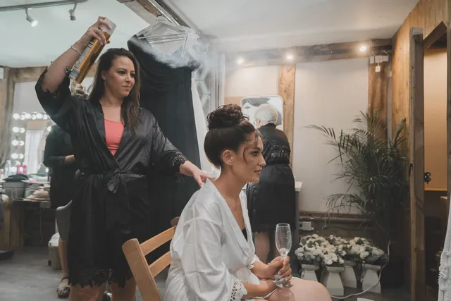 A bridesmaid having her makeup finished with a glass of fizz
