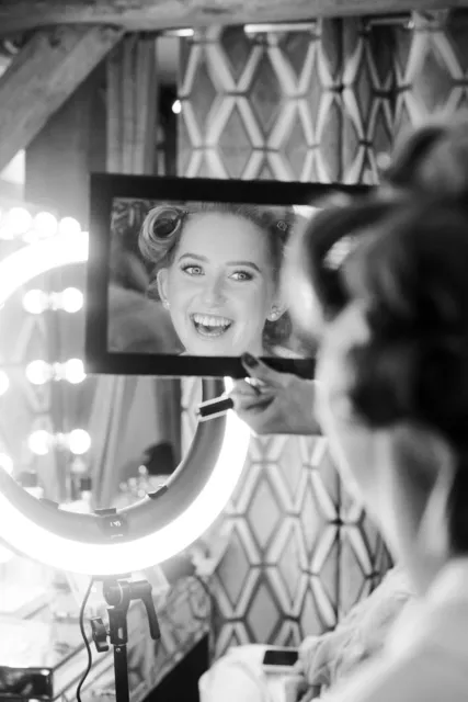 A bride laughing in the lit vanity mirror