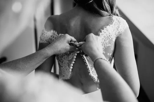 A bride's dress being buttoned in black and white