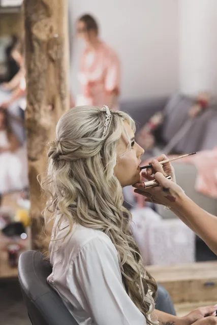 A bride having her makeup finished by the window