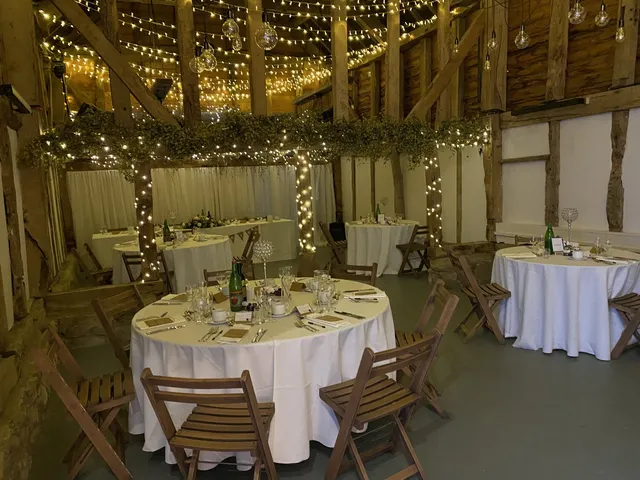 Round tables dressed for a party beneath the barn's fairy lights