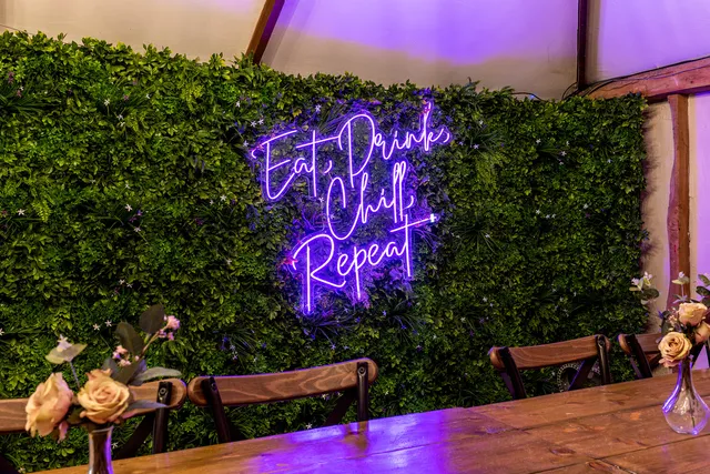 An 'Eat Drink Chill Repeat' neon sign on a greenery wall