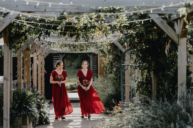 Bridesmaids in red walking the pergola aisle