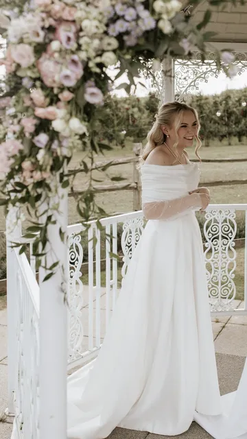 A bride beside the gazebo's white ironwork, framed by florals