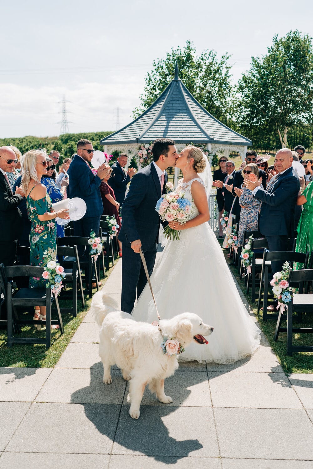 A couple kiss surrounded by guests in the Orchard Garden