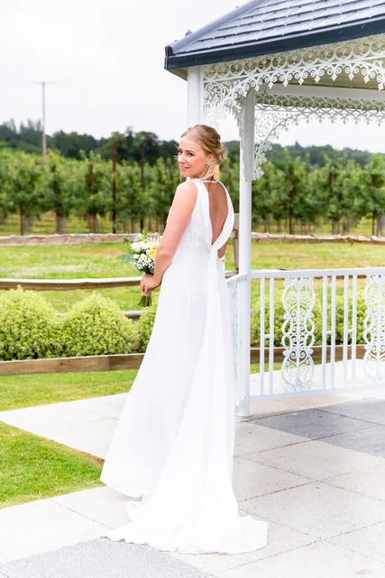 A bride looks back over her shoulder at the Orchard Garden gazebo