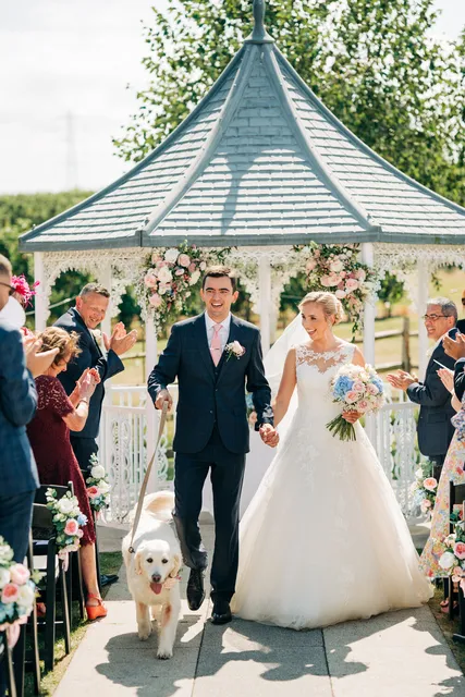 A couple leave their ceremony with their dog at the gazebo