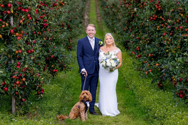 A couple with their cockapoo between the apple trees