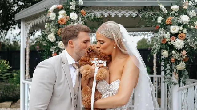 A couple kiss their dog beneath a floral arch