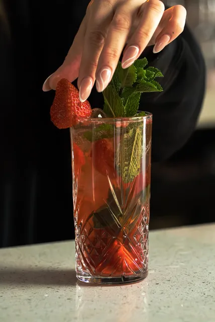 A bartender garnishing a tall summer cocktail with strawberry and mint