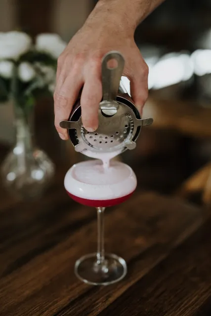 A cocktail being strained into a chilled coupe