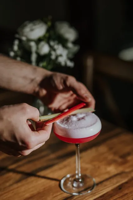 A foam topped cocktail being finished with a rhubarb garnish