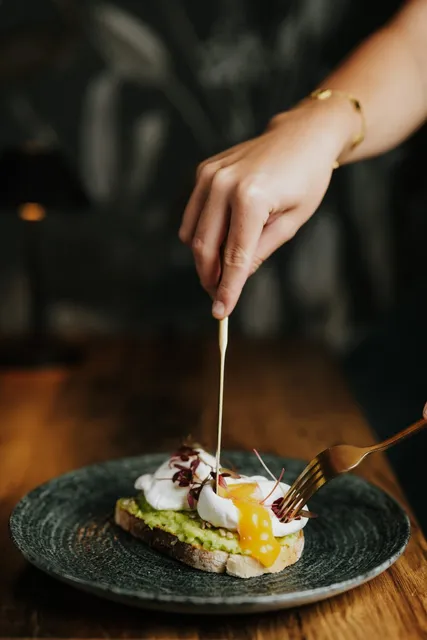 A poached egg dish being finished by hand