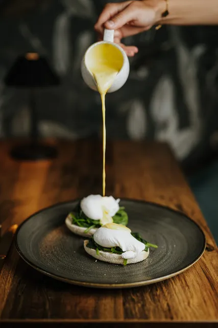 Hollandaise being poured over poached eggs