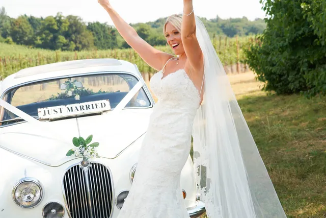 A bride cheering beside the wedding car