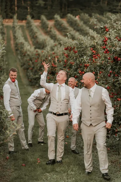 Groomsmen larking about among the apple trees