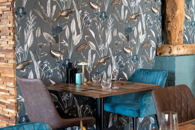 A booth table at The Rooster with teal velvet seating and botanical wallpaper