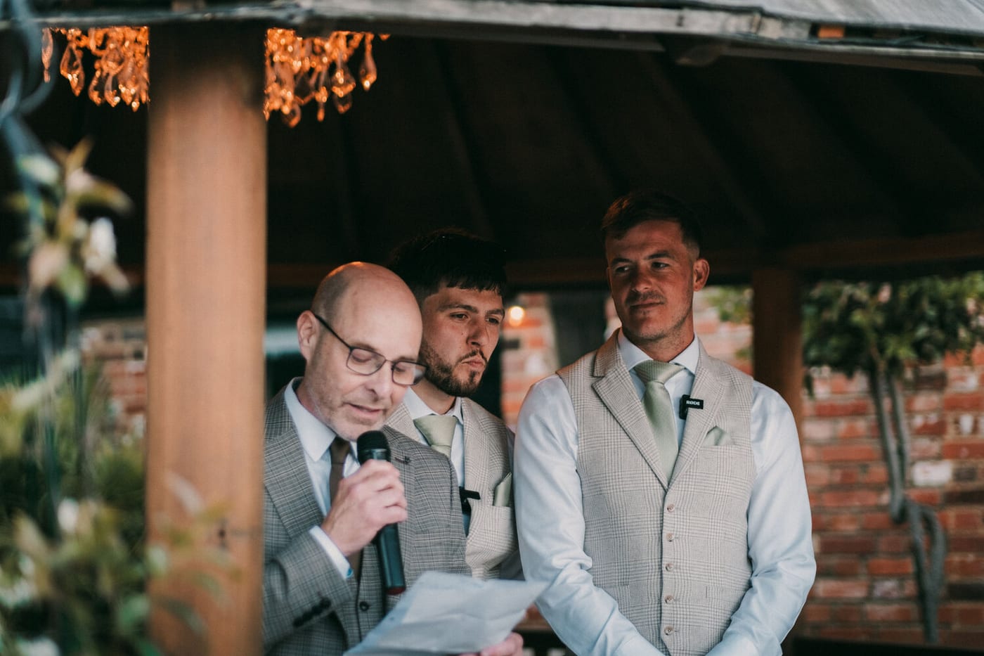 A father of the bride giving a speech under the gazebo at The BarnYard, with two of the wedding party listening