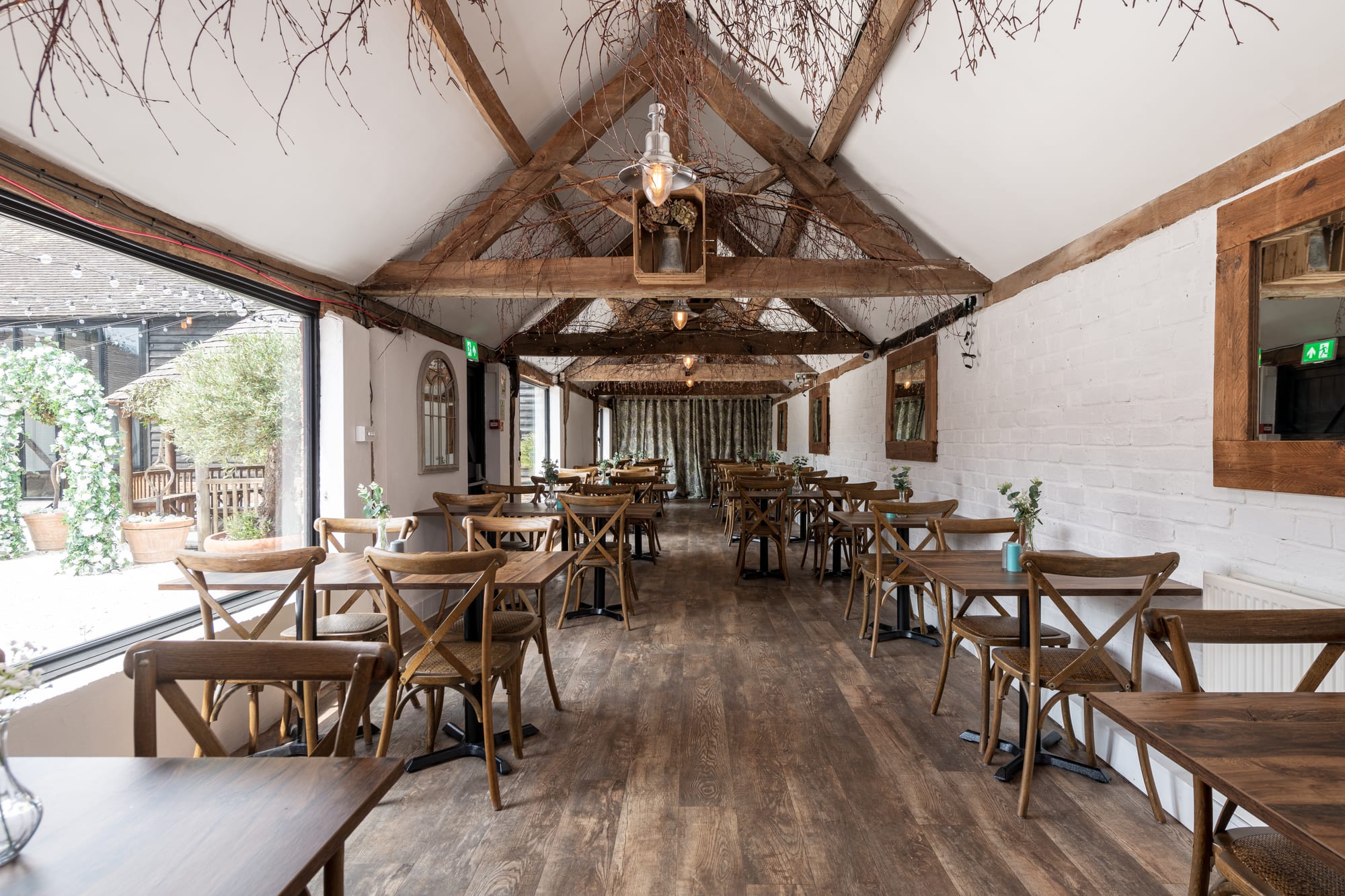 The Roost at The BarnYard, a light oak-beamed room with round tables and doors open onto the gardens