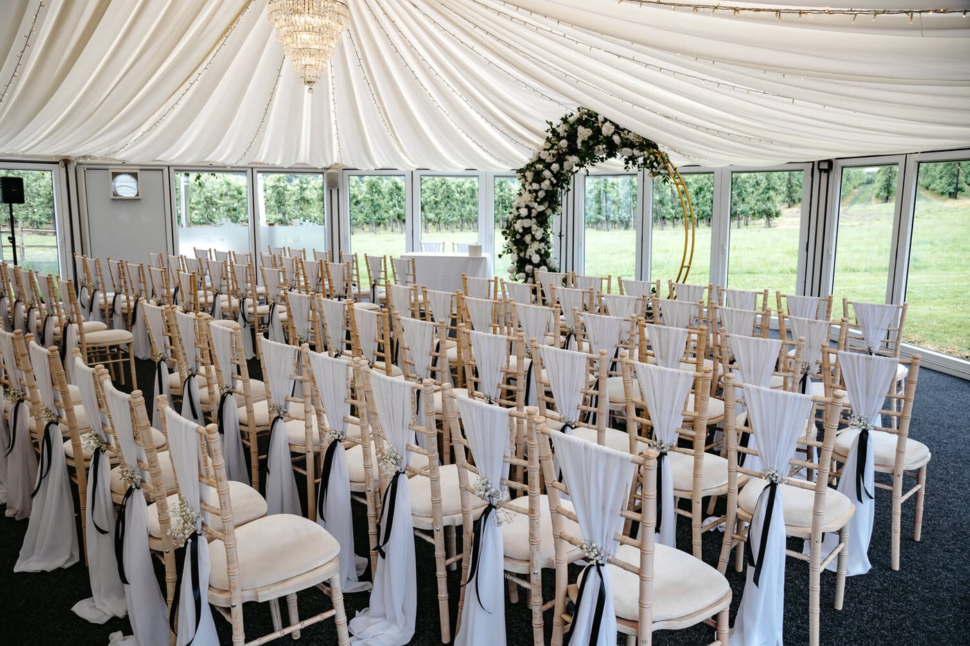 The indoor ceremony area inside The Arboretum at The BarnYard, with curved glass doors onto the orchards