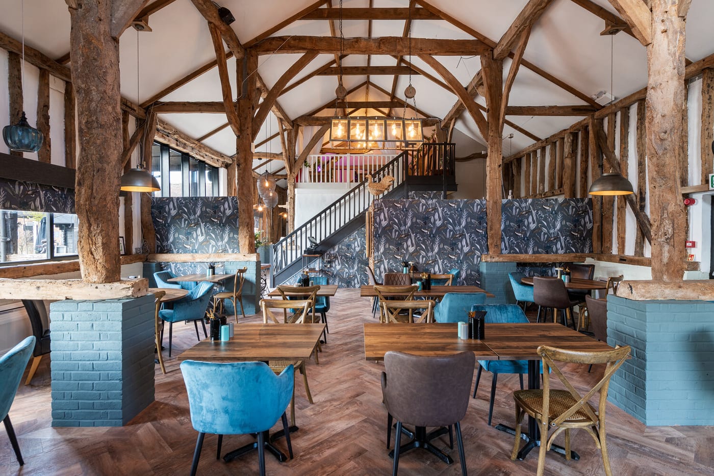 The oak-beamed dining room of The Rooster restaurant at The BarnYard, with herringbone floors and teal chairs