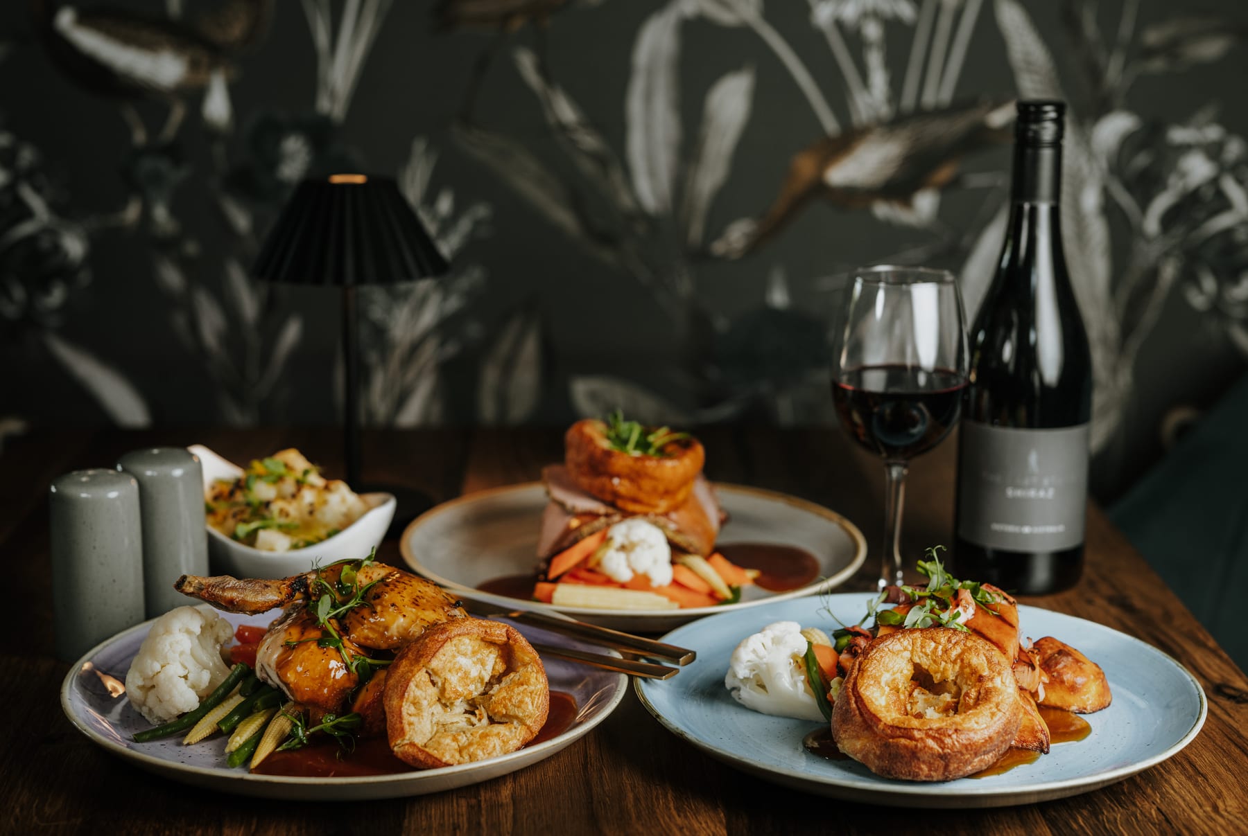 A table laid for Sunday lunch at The BarnYard, with roasts, Yorkshire puddings and a glass of red wine