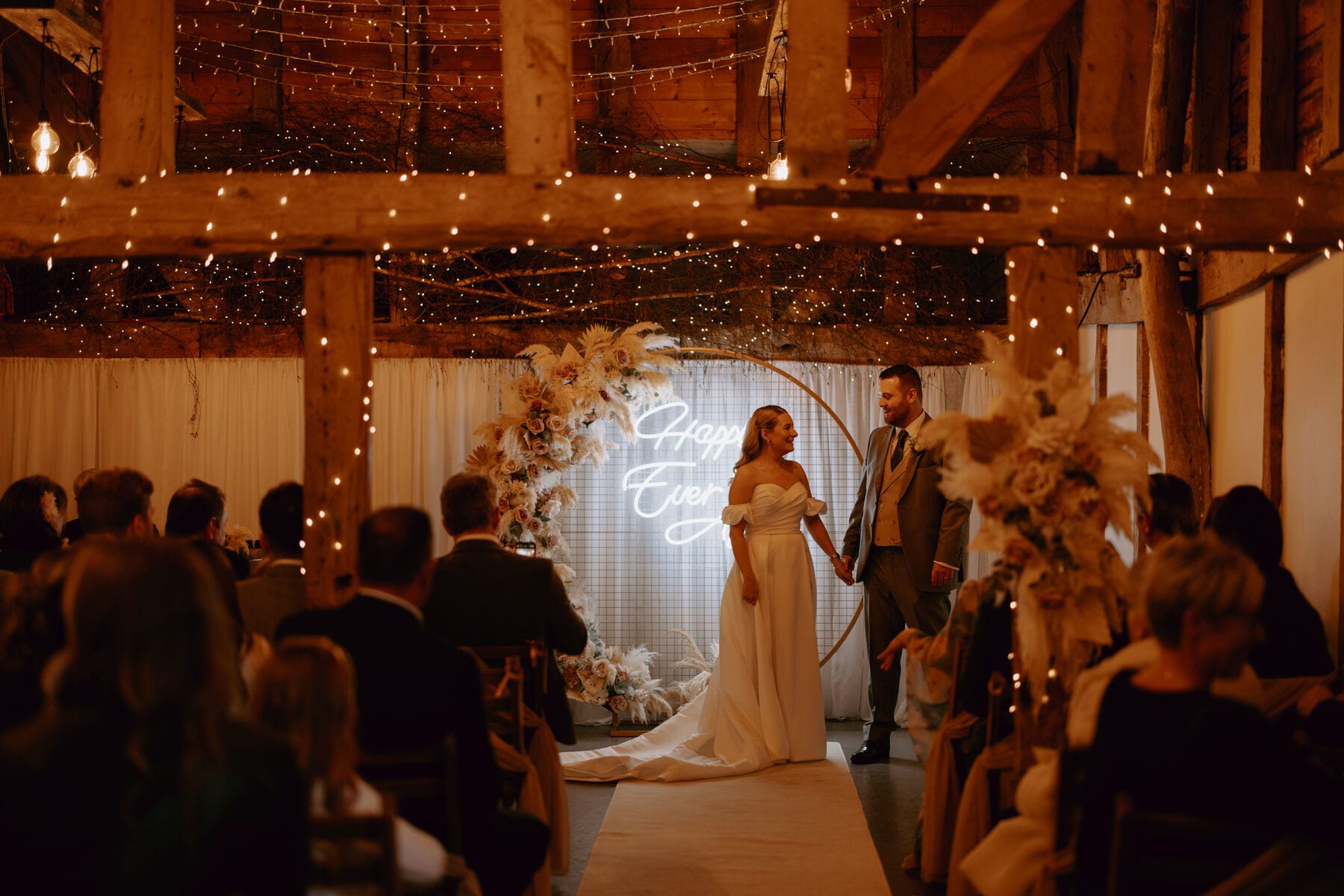 A couple at their wedding ceremony in the fairy-lit Apple Barn at The BarnYard, Kent