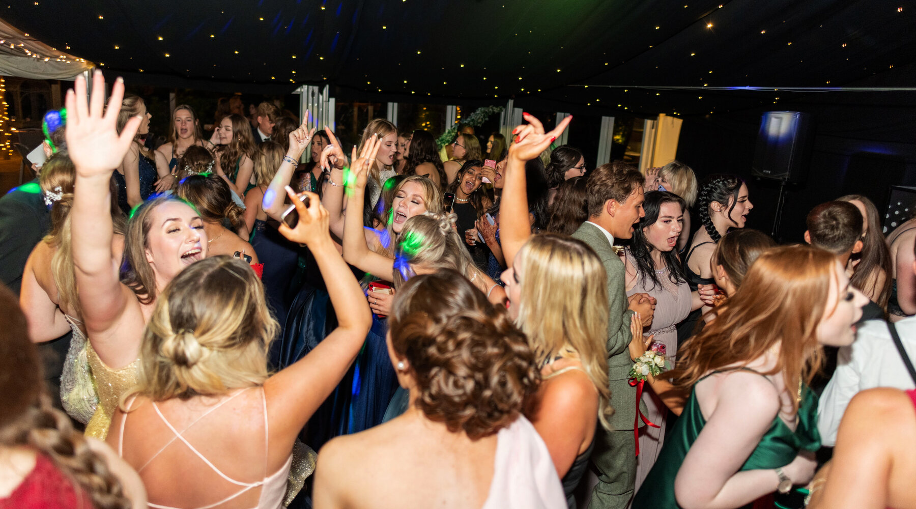 A packed prom dancefloor at The BarnYard, students singing with their hands in the air